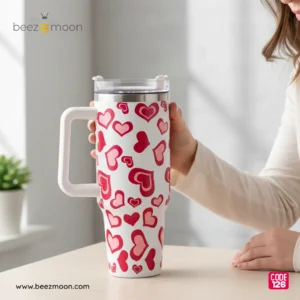 Large white 'Stanley-style' insulated tumbler with a dense, all-over pattern of varied red and pink hearts, a sturdy white ergonomic handle, and a clear flip-straw lid, isolated on a light background. Features "Big size" and "Heavy Duty" build.