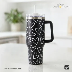 Heavy-duty black 'Stanley-style' insulated tumbler with a white heart print pattern, featuring a large ergonomic handle and clear straw, branded Beezmoon Code 127.